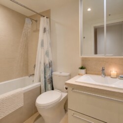 Modern bathroom with a tub, rainfall showerhead, and patterned shower curtain beside a white toilet and beige tiled walls.