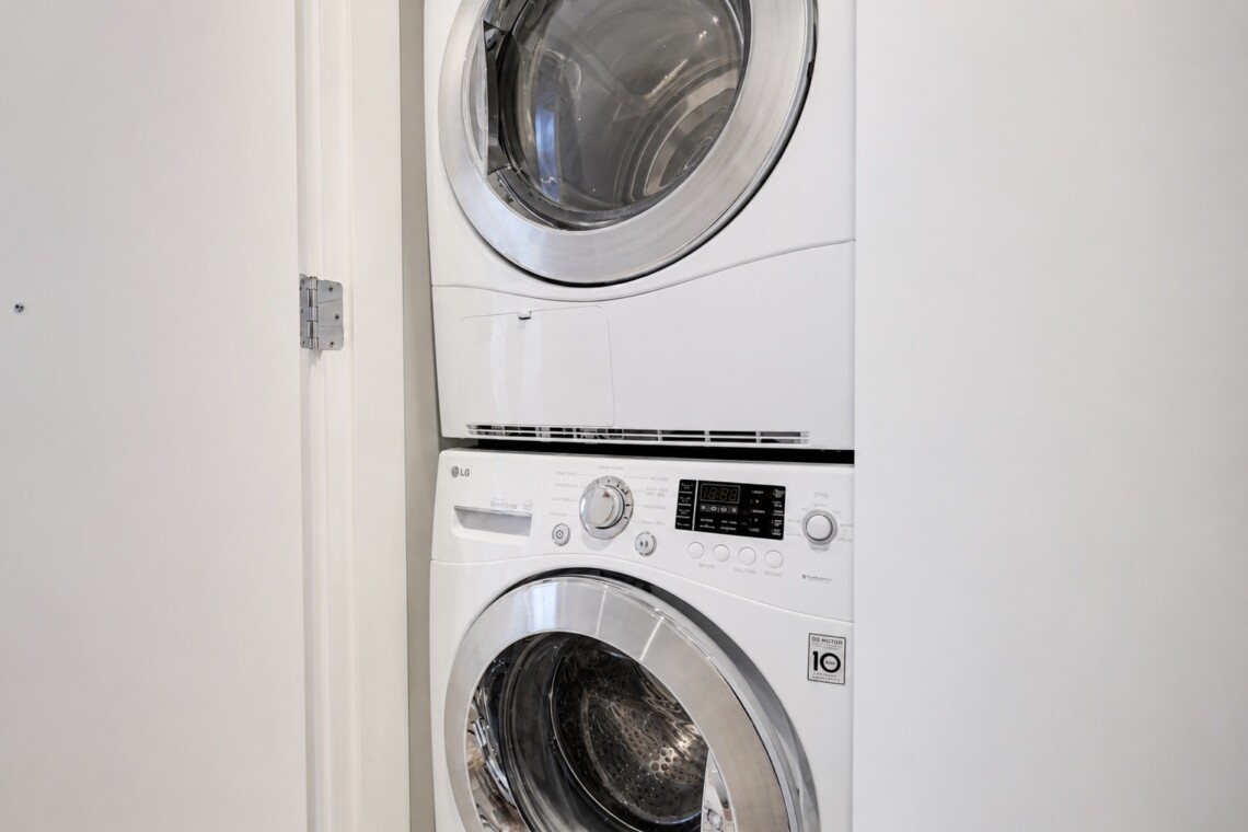 Front-loading washer and dryer stacked in a narrow laundry alcove/closet with white front panels and chrome doors.