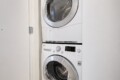 Front-loading washer and dryer stacked in a narrow laundry alcove/closet with white front panels and chrome doors.