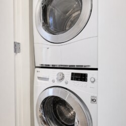Front-loading washer and dryer stacked in a narrow laundry alcove/closet with white front panels and chrome doors.