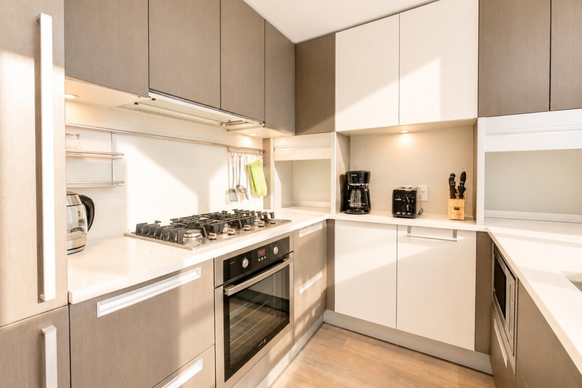 Modern U-shaped kitchen with beige upper cabinets, white countertops, gas stove, and built-in oven.