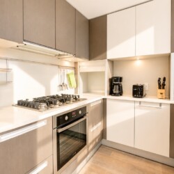 Modern U-shaped kitchen with beige upper cabinets, white countertops, gas stove, and built-in oven.
