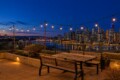 Rooftop patio at dusk with string lights and wooden table and bench, overlooking a city skyline across the water.
