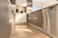 Modern kitchen with stainless steel appliances, wood-textured cabinets, and sunlight from a window.