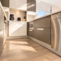 Modern kitchen with stainless steel appliances, wood-textured cabinets, and sunlight from a window.