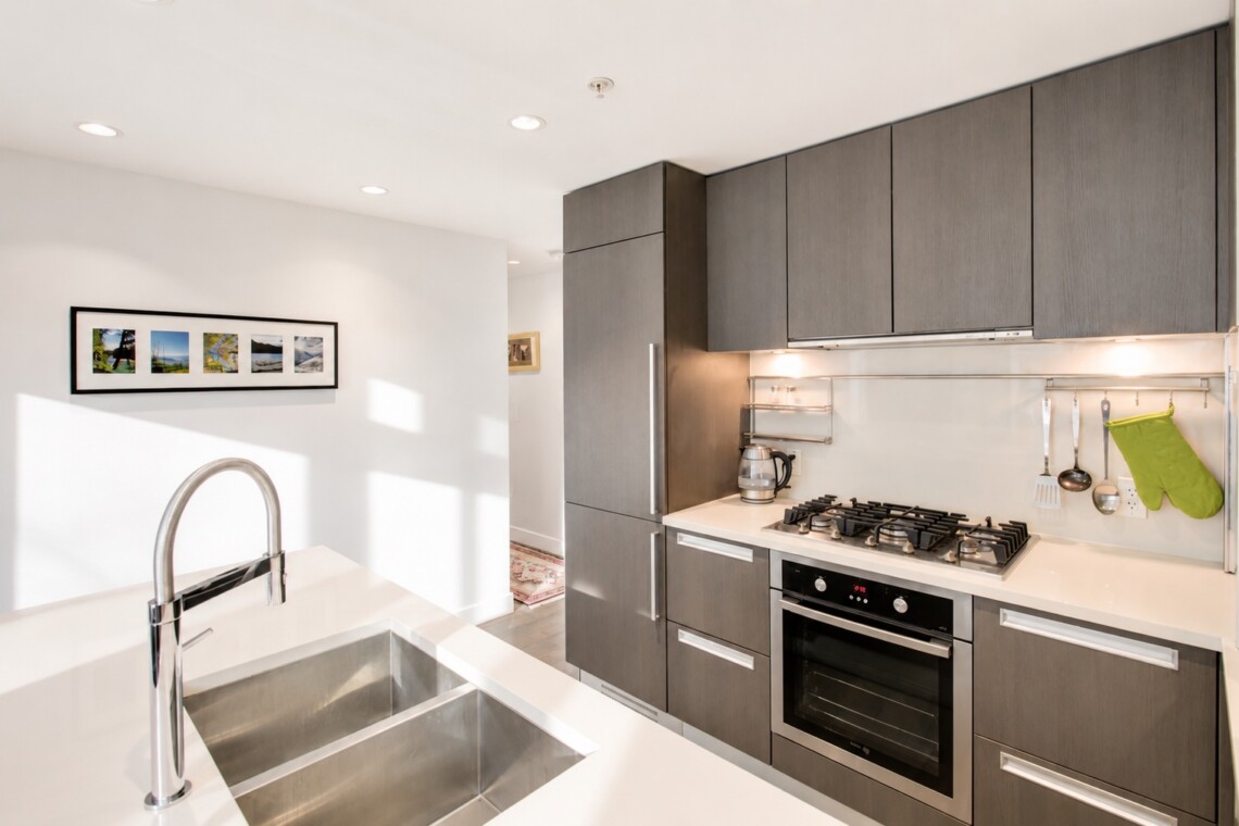 Modern kitchen with gray cabinetry, white countertops and a stainless steel double-basin sink on an island.