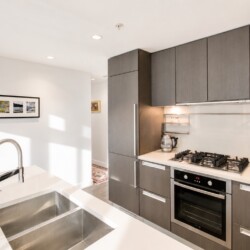 Modern kitchen with gray cabinetry, white countertops and a stainless steel double-basin sink on an island.