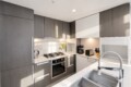 Modern kitchen with gray and white cabinetry, stainless appliances, and a large chrome sink in the foreground.