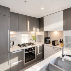 Modern kitchen with gray and white cabinetry, stainless appliances, and a large chrome sink in the foreground.