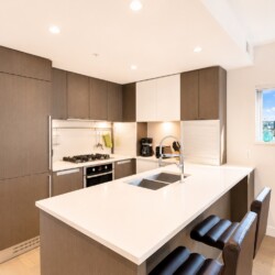 Modern kitchen with white island, double sink, and gray cabinets; large window shows a cityscape outside.