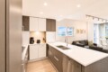 Open-concept kitchen with white and gray cabinets, an island sink, and stainless appliances adjoining a living room with a gray sofa and framed art.