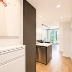 Open-concept kitchen and living area with white cabinetry, a stainless dishwasher, dark island, and lighthouse artwork on the wall.