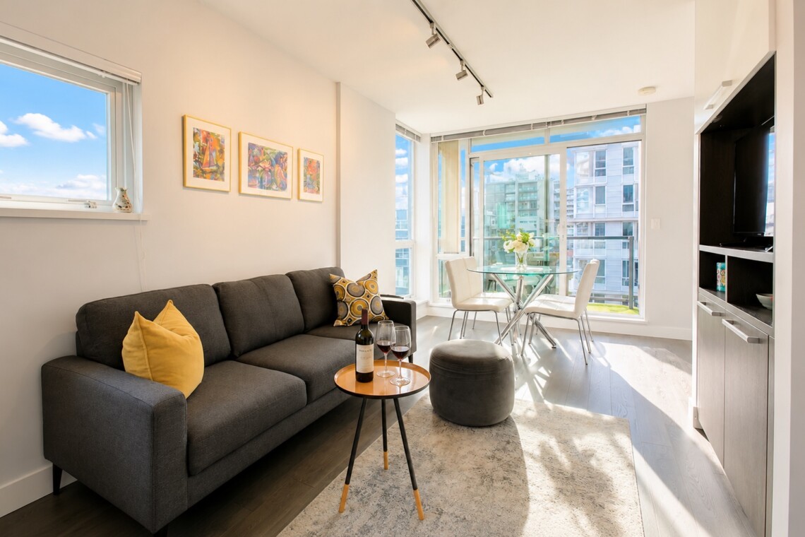 Bright living room with a gray sofa, yellow cushions, a round table with a wine bottle and two glasses.