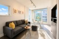 Bright living room with a gray sofa, yellow cushions, a round table with a wine bottle and two glasses.