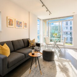 Bright living room with a gray sofa, yellow cushions, a round table with a wine bottle and two glasses.