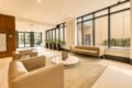 Modern hotel lobby with beige leather sofas, a round glass coffee table, and large floor-to-ceiling windows with potted plants along the wall.