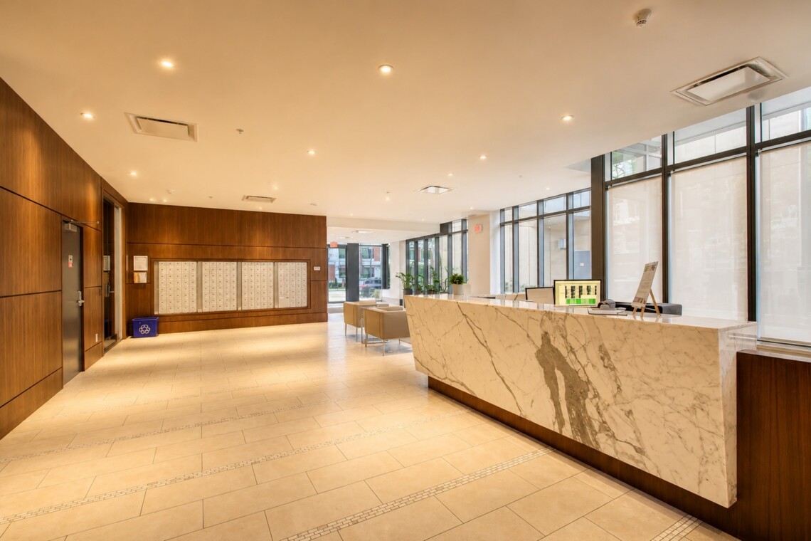 Bright hotel-style lobby with a marble reception desk, wood-paneled walls, and large windows offering natural light.