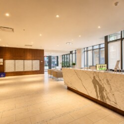 Bright hotel-style lobby with a marble reception desk, wood-paneled walls, and large windows offering natural light.