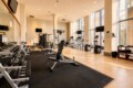 Well-lit gym with free weights, benches, treadmills, and bikes along large windows at the back of the room.