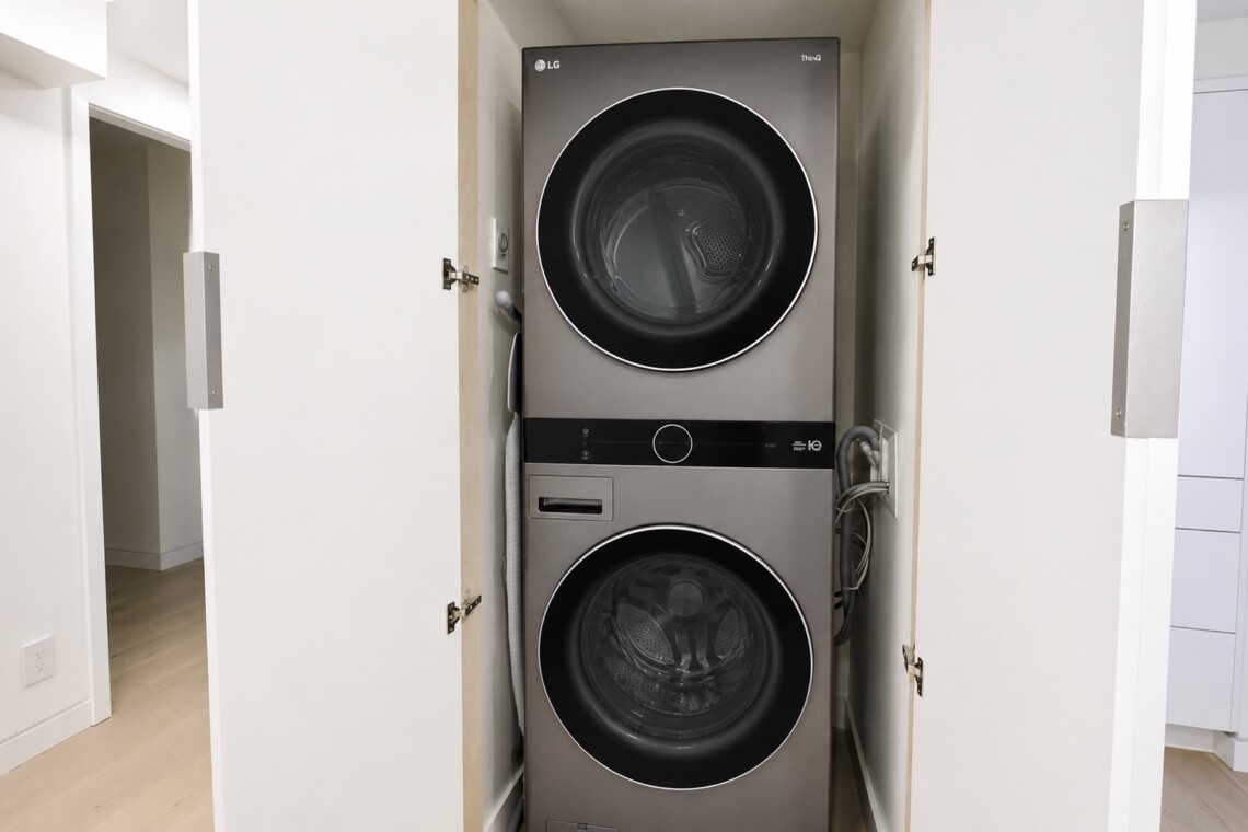 Stacked front-loading washer and dryer in a small closet with doors open, silver-gray finish visible.