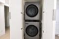 Stacked front-loading washer and dryer in a small closet with doors open, silver-gray finish visible.