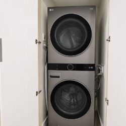 Stacked front-loading washer and dryer in a small closet with doors open, silver-gray finish visible.