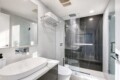 Modern bathroom with glass shower enclosure, white vessel sink, and chrome fixtures against light gray walls and a large mirror.
