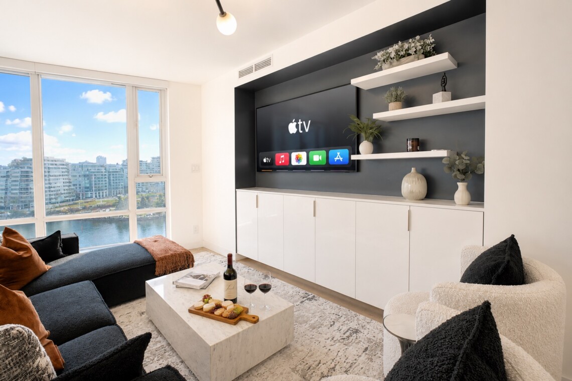 Modern living room with a wall-mounted Apple TV and built-in white cabinets beneath, navy accent wall, and open shelves with plants.
