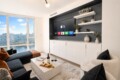 Modern living room with a wall-mounted Apple TV and built-in white cabinets beneath, navy accent wall, and open shelves with plants.