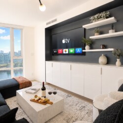 Modern living room with a wall-mounted Apple TV and built-in white cabinets beneath, navy accent wall, and open shelves with plants.