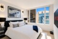 Modern hotel bedroom with white bedding, black headboard, abstract wall art, and side lamps.