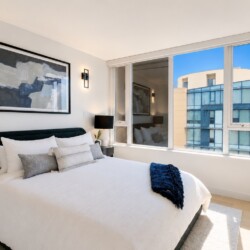 Modern hotel bedroom with white bedding, black headboard, abstract wall art, and side lamps.