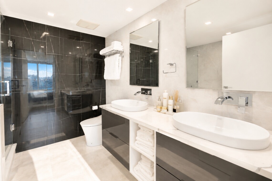 Modern bathroom with a double vanity, two round vessel sinks, and large mirrors over a white countertop. Glass-walled shower on the left.