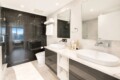 Modern bathroom with a double vanity, two round vessel sinks, and large mirrors over a white countertop. Glass-walled shower on the left.