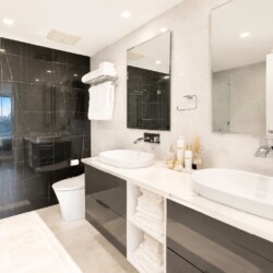 Modern bathroom with a double vanity, two round vessel sinks, and large mirrors over a white countertop. Glass-walled shower on the left.
