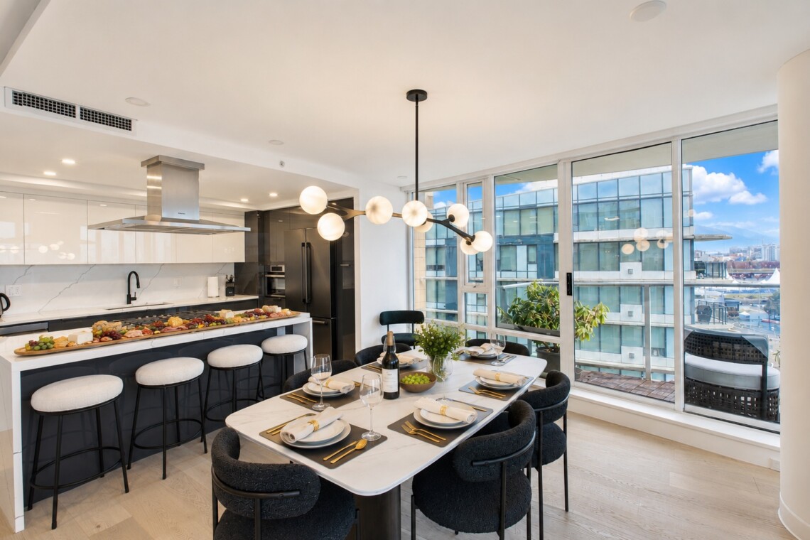 Open-plan kitchen and dining area with a marble table set for eight, gold cutlery, and a city skyline view through large windows.