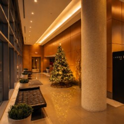 Modern hotel lobby with a tall christmas tree, warm golden lighting, and a black tufted bench by glass walls.