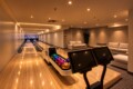 Indoor bowling alley with polished wooden lanes, a ball return displaying colorful bowling balls, and a seating area with white couches in the background.