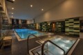 Indoor swimming pool area in a spa with green tiled walls, metal handrails, and a connected hot tub in the foreground.