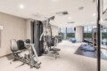 Modern gym with a multi-station weight machine, benches, dumbbells, and a blue exercise ball near large windows.