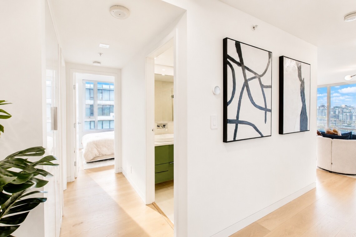 Bright, minimalist apartment hallway with a doorway to a bedroom and a bathroom, and large abstract black-and-white art on the right wall.