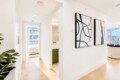 Bright, minimalist apartment hallway with a doorway to a bedroom and a bathroom, and large abstract black-and-white art on the right wall.