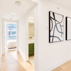 Bright, minimalist apartment hallway with a doorway to a bedroom and a bathroom, and large abstract black-and-white art on the right wall.