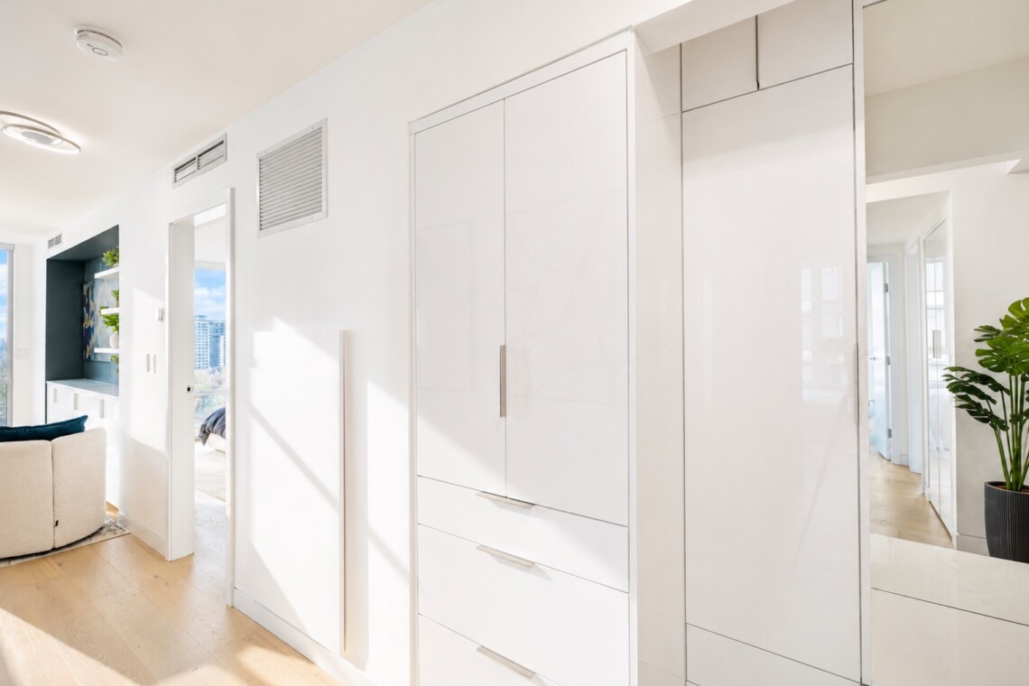 Bright modern interior with white built-in cabinets along a hallway; natural light from large windows and a plant in the corner.