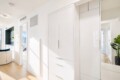 Bright modern interior with white built-in cabinets along a hallway; natural light from large windows and a plant in the corner.