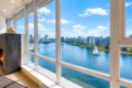 Living room with a marble fireplace and large windows overlooking a river, sailboat, and city skyline.