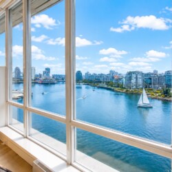 Living room with a marble fireplace and large windows overlooking a river, sailboat, and city skyline.