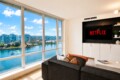 Modern living room with oversized windows offering a river and city view; Netflix is displayed on the wall TV.