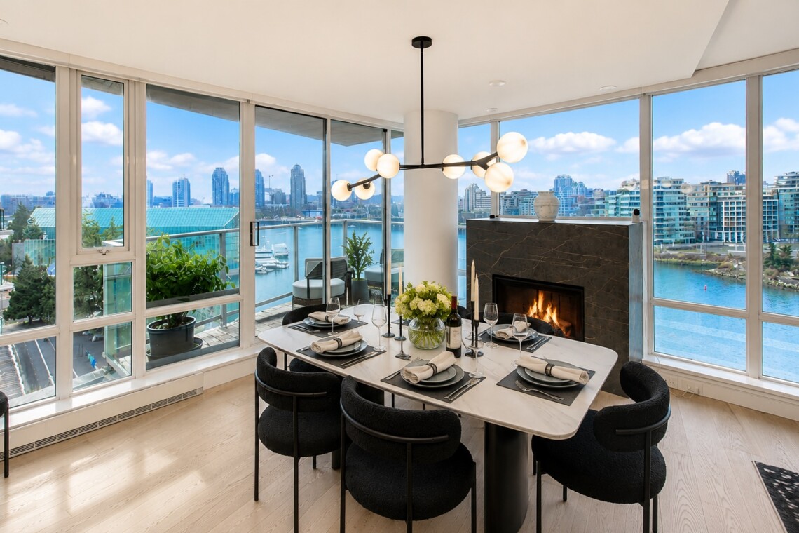 Modern dining room with a marble table for six, a contemporary chandelier, and a fireplace, overlooking a waterfront city skyline.