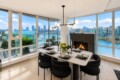 Modern dining room with a marble table for six, a contemporary chandelier, and a fireplace, overlooking a waterfront city skyline.